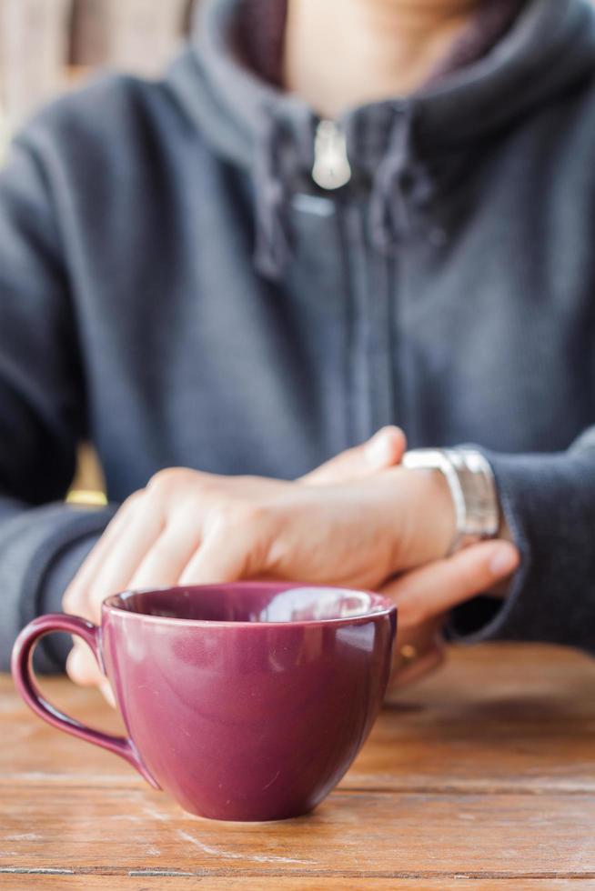 Taza de café púrpura en una mesa frente a una persona foto