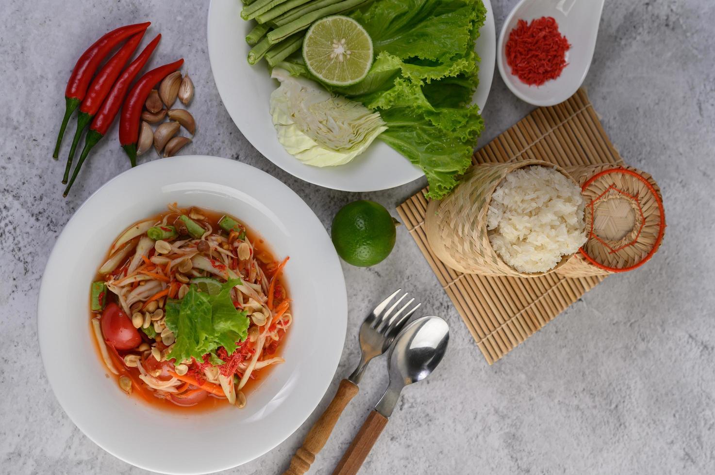 Thai papaya salad in a white plate with Sticky rice, Spoon, fork, and dried shrimp. photo