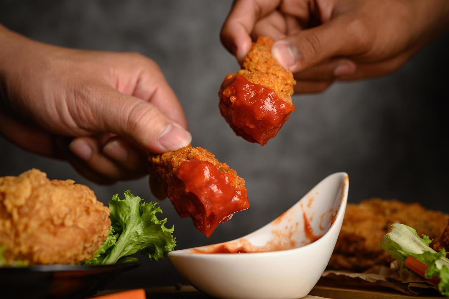 Two hands holding crispy chicken tenders in tomato sauce photo