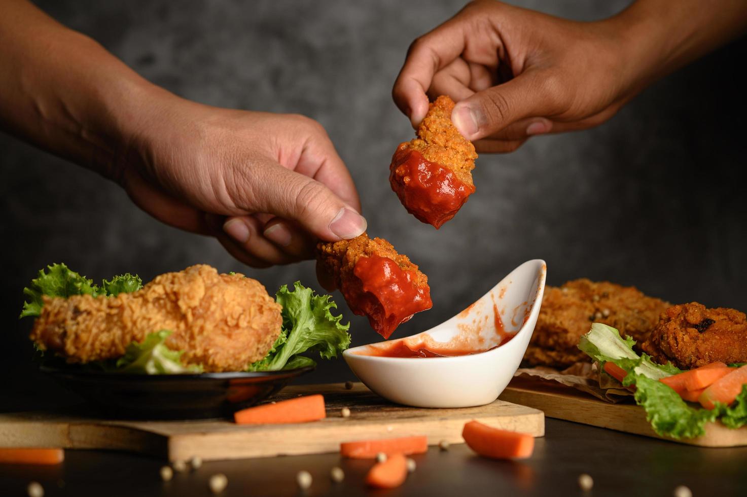 Dos manos sosteniendo ofertas de pollo crujiente en salsa de tomate foto