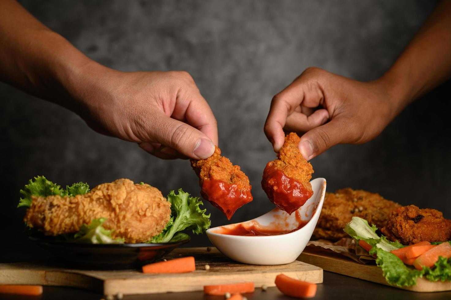 Dos manos sosteniendo ofertas de pollo crujiente en salsa de tomate foto