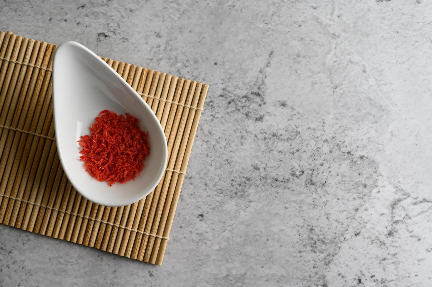 Small red dried shrimp in a cup on a wooden mat photo