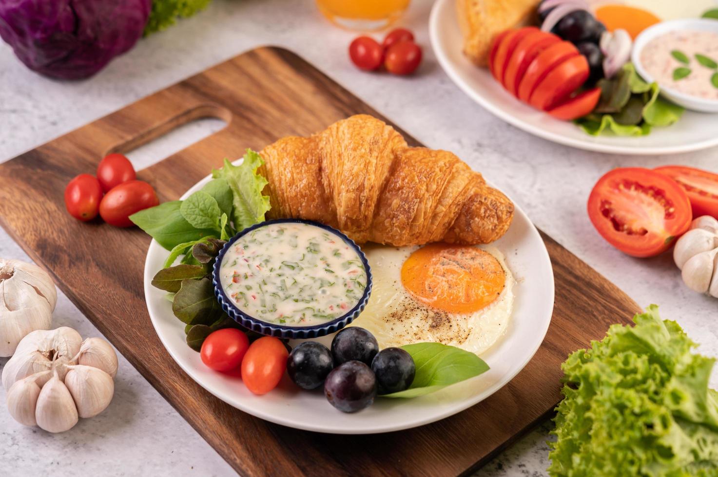 Croissant, fried egg, salad dressing, black grapes, and tomatoes photo