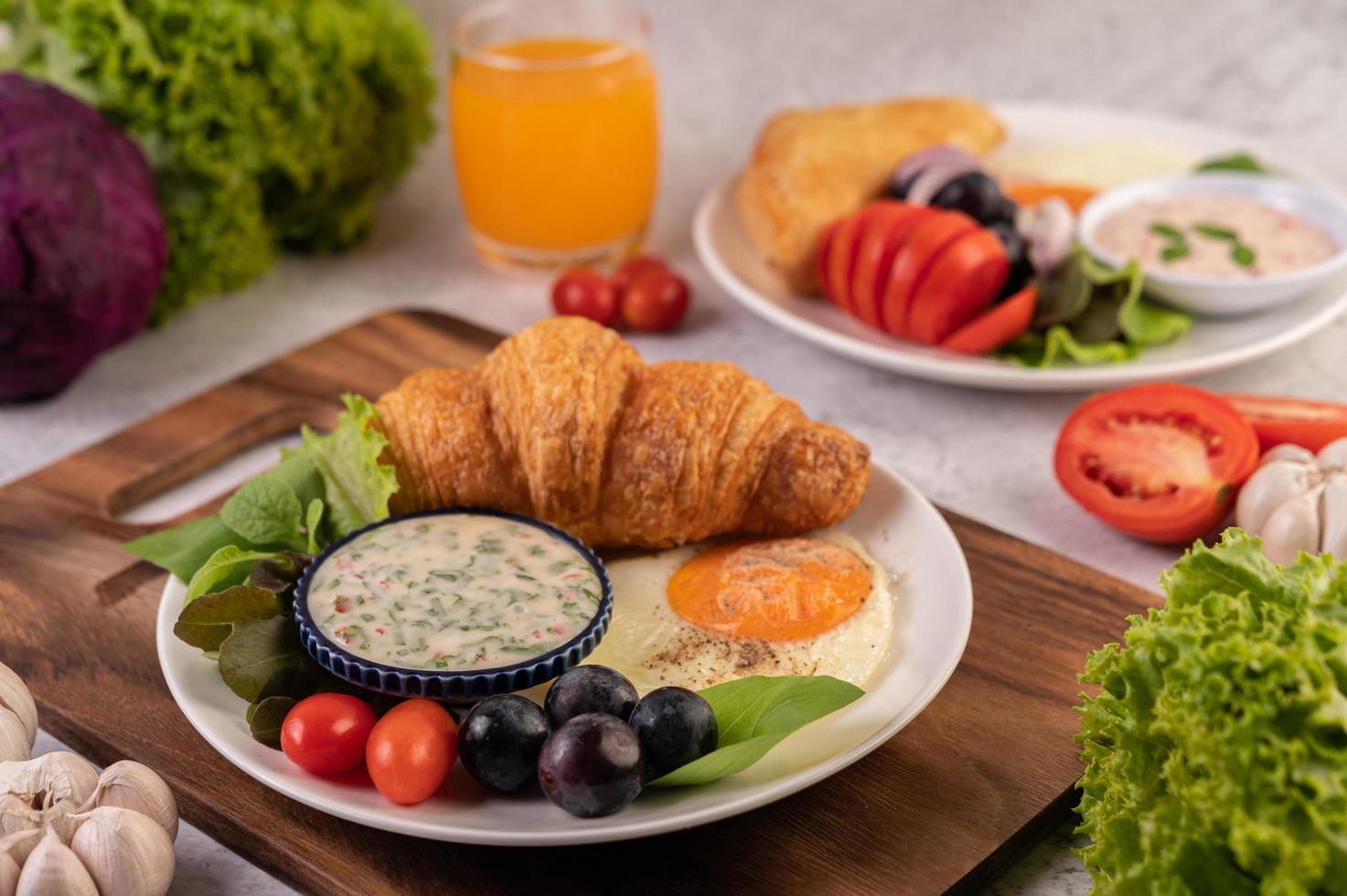 Croissant, fried egg, salad dressing, black grapes, and tomatoes photo