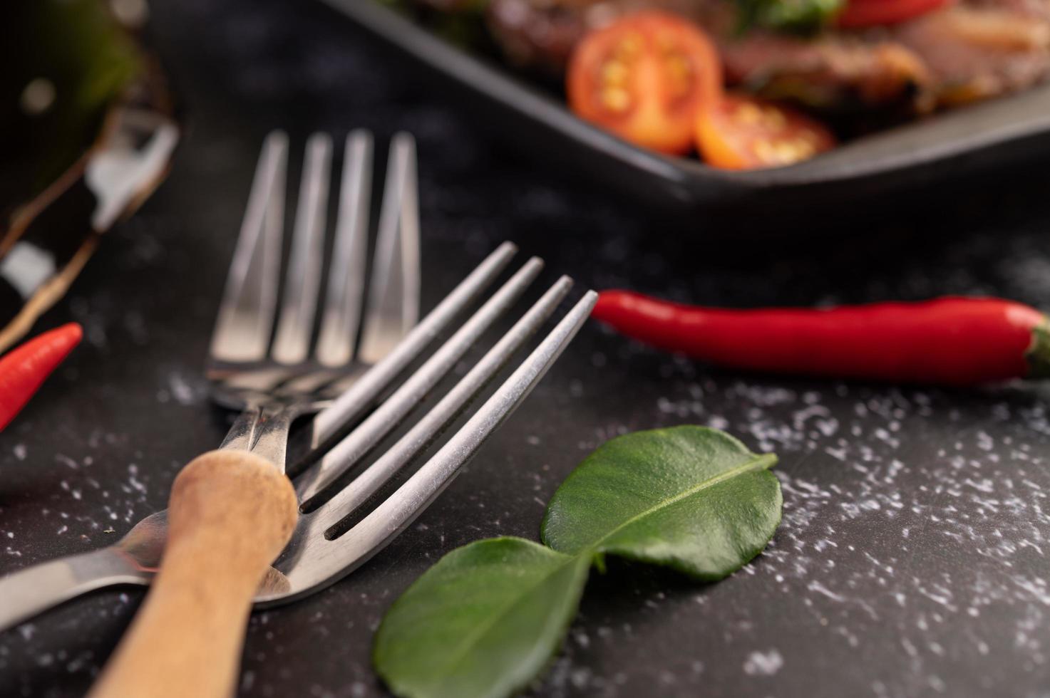 Two forks with chili and kaffir lime leaves on a black background photo