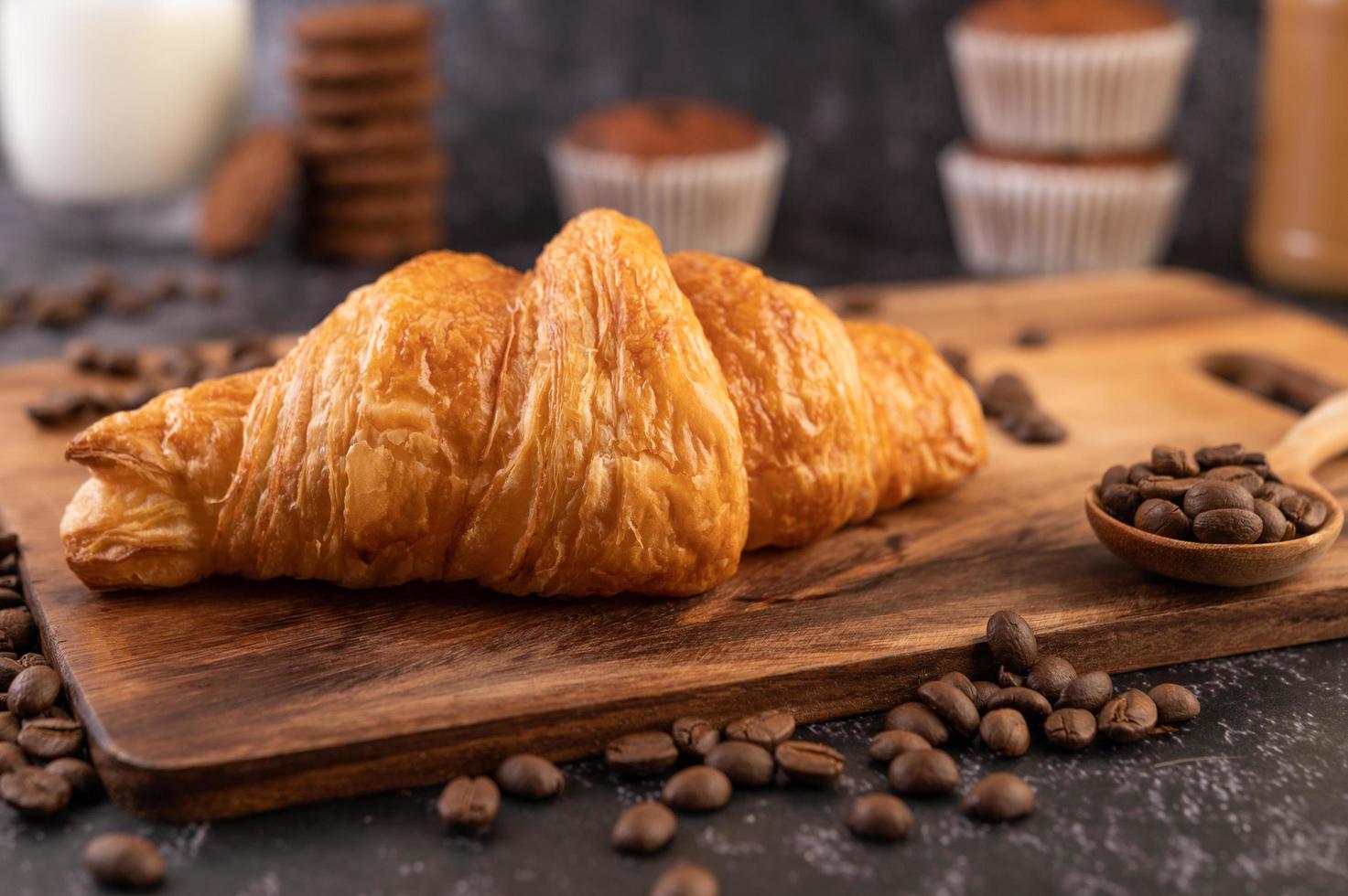 Croissant sobre una tabla de madera con granos de café. foto
