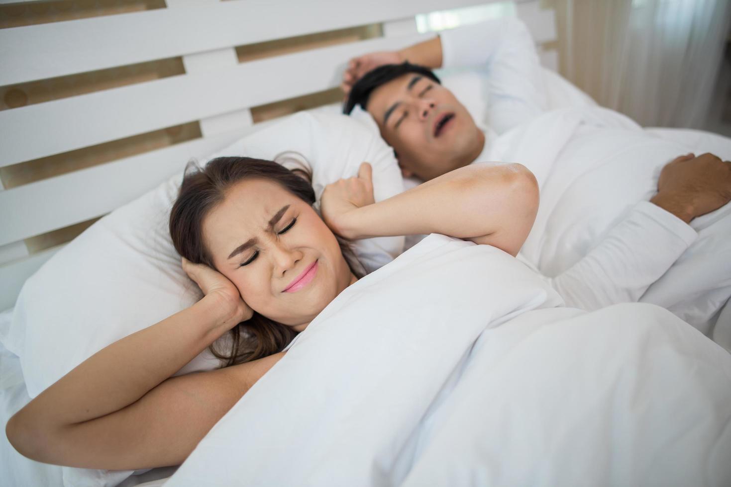 Sleeping woman blocking ears with man snoring in bed photo