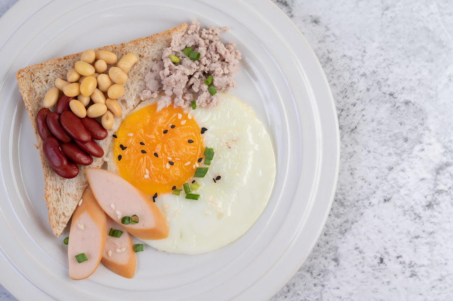 Fried eggs, sausage, minced pork, bread and red beans photo