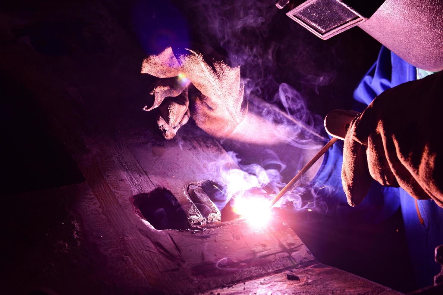 Soldador en uniforme azul soldando la pieza de trabajo foto