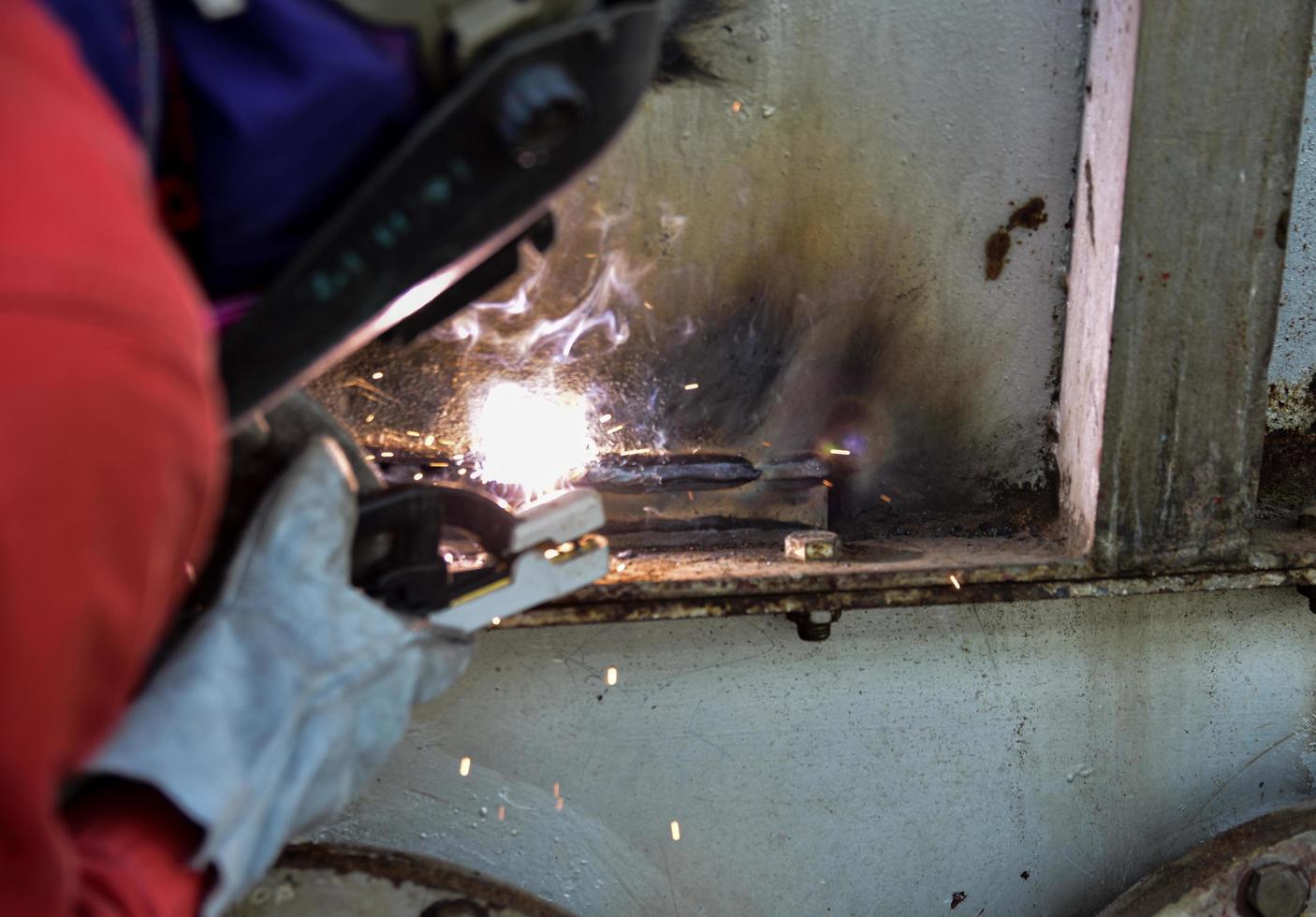 Welder in red suite welding the steel casing of the factory photo