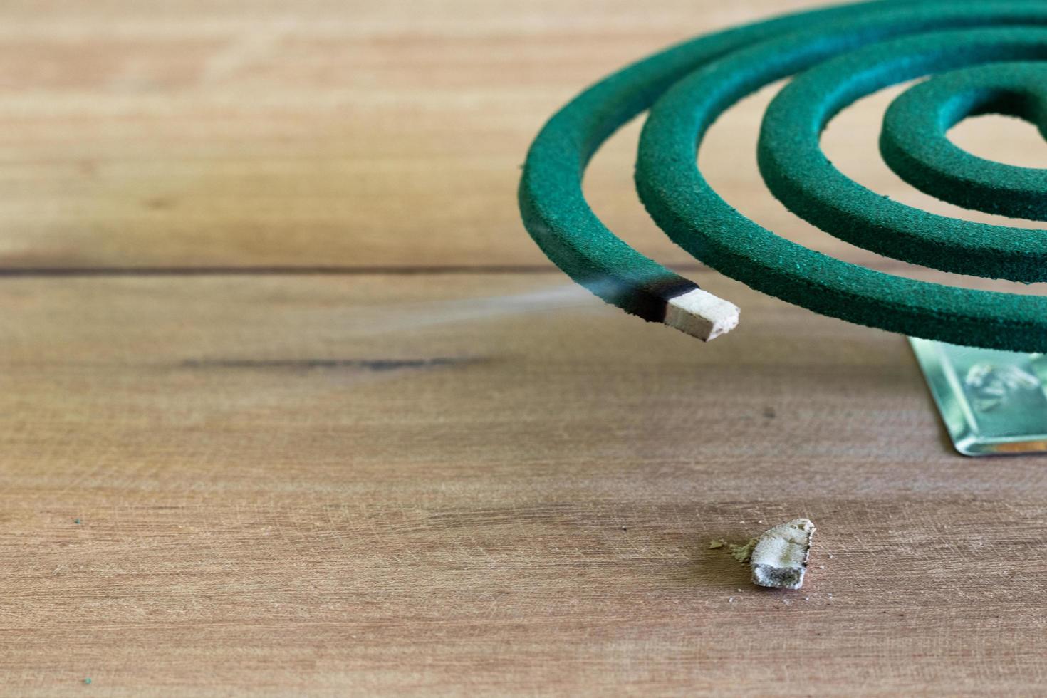 Repelente de mosquitos verde ardiendo y humo blanco en la mesa de madera con luz verde borrosa. foto