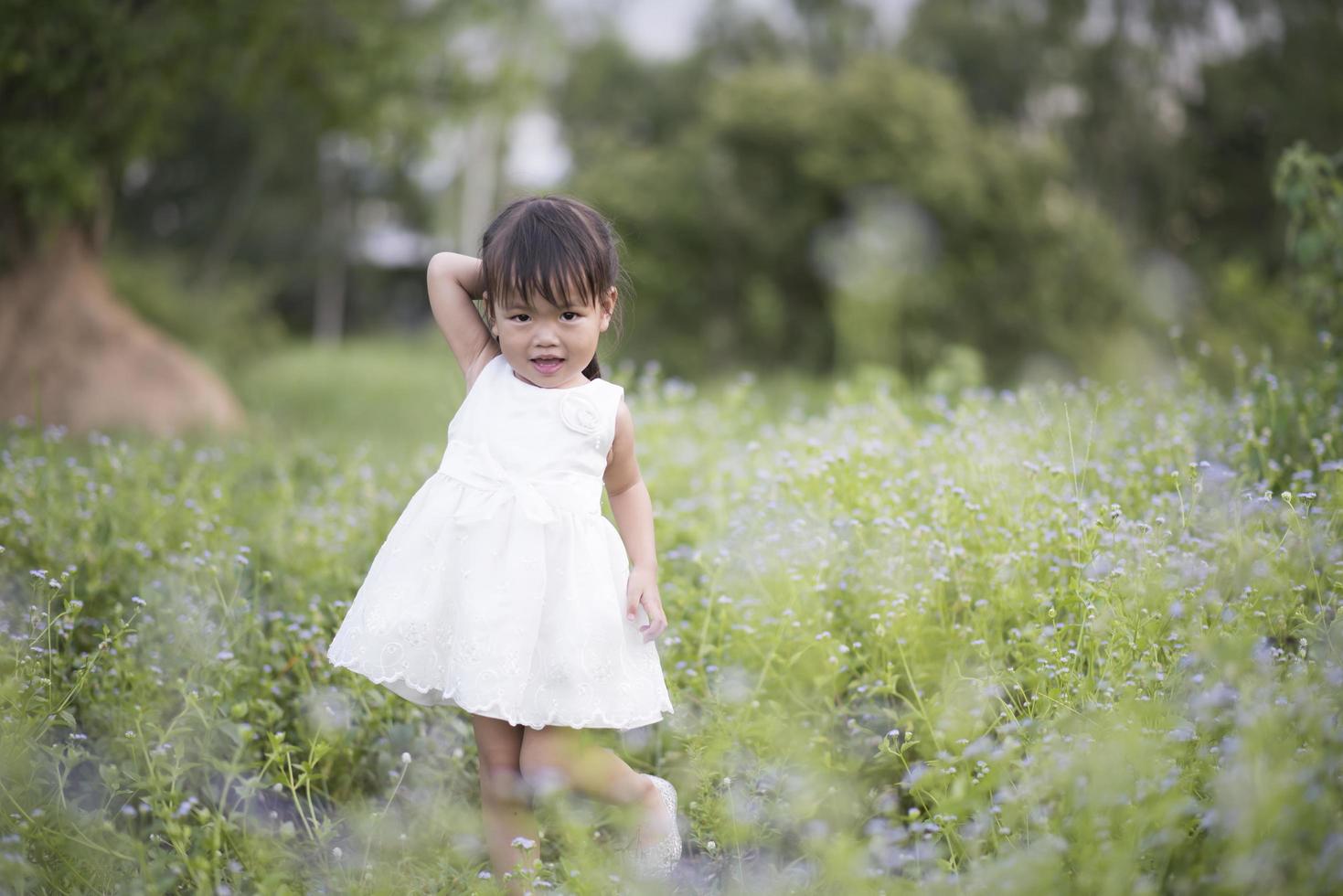 Happy little girl standing in the meadow in a white dress photo