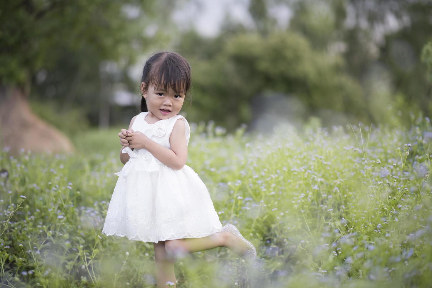 Happy little girl standing in the meadow in a white dress photo