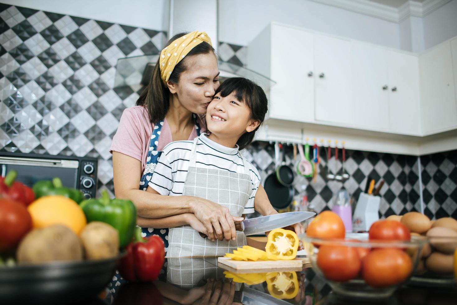 Happy mom and daughter preparing and chopping vegetables in the kitchen photo