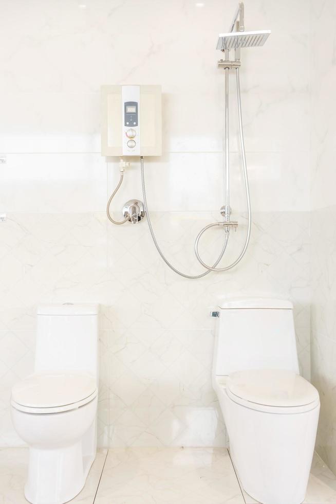 Interior de baño con ducha. Calentador de agua e inodoro en la pared de azulejos blancos foto