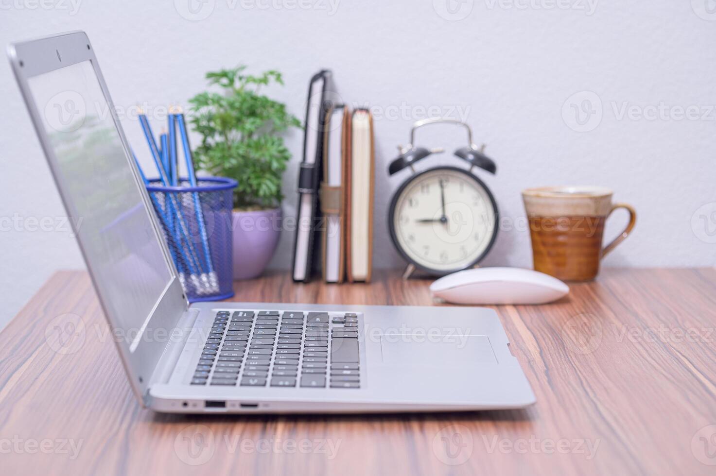 A laptop computer sitting on a desk next to a clock photo