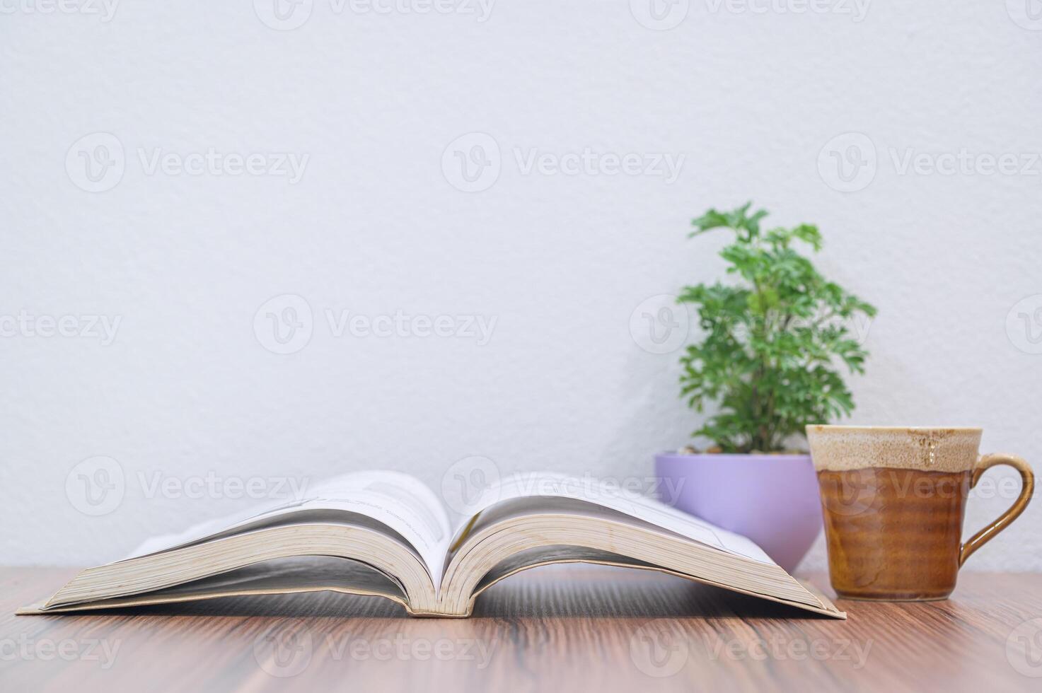 Open book and coffee mug on wooden table with white wall background photo
