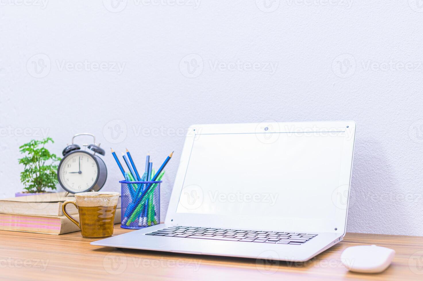 A laptop on a desk with a clock, coffee mug, and books photo