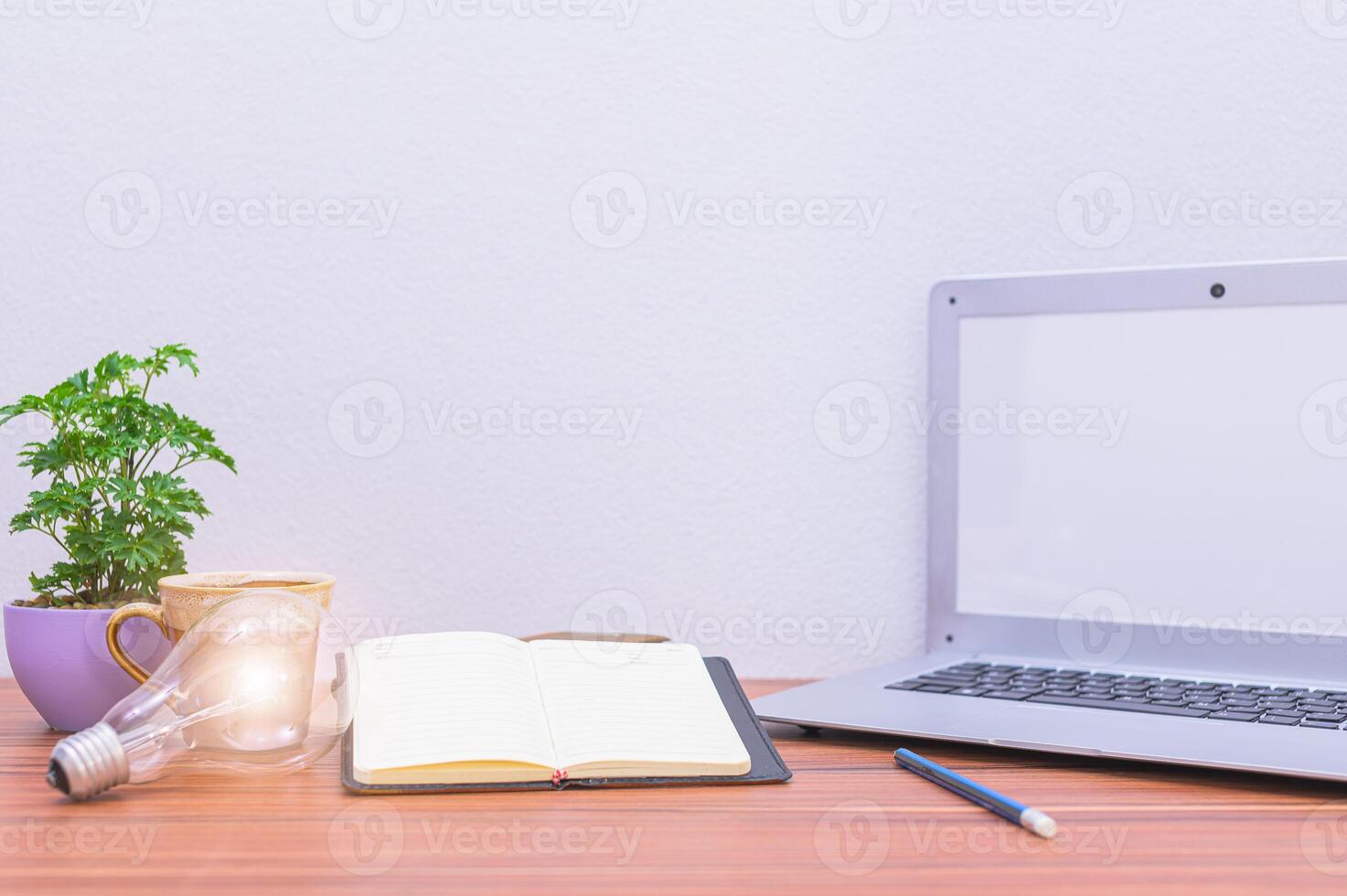 Laptop on wooden desk with notebook, plant and lamp photo
