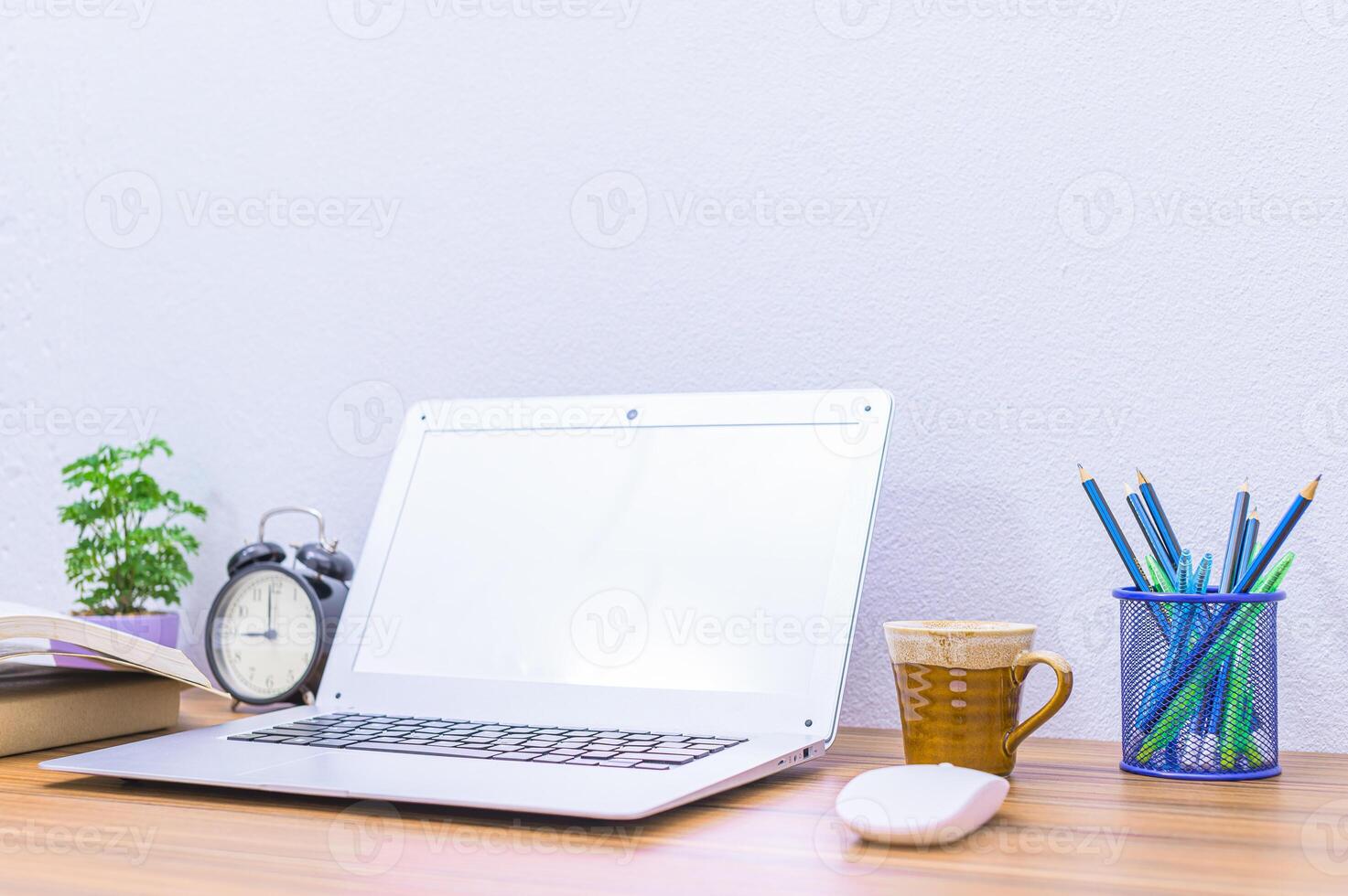 A laptop on a desk with a clock, pencils, and a plant photo