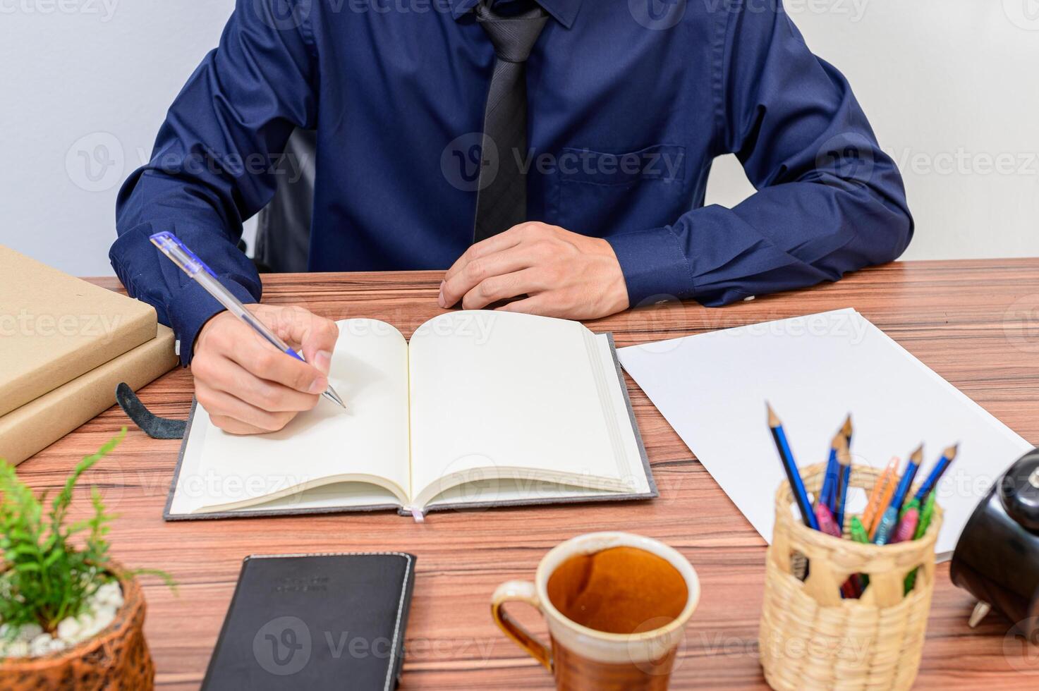 A man in a blue shirt is sitting at a desk with a notebook and pen photo