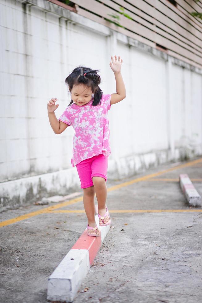 Little asian girl walking on the curb and trying to keep her balance photo