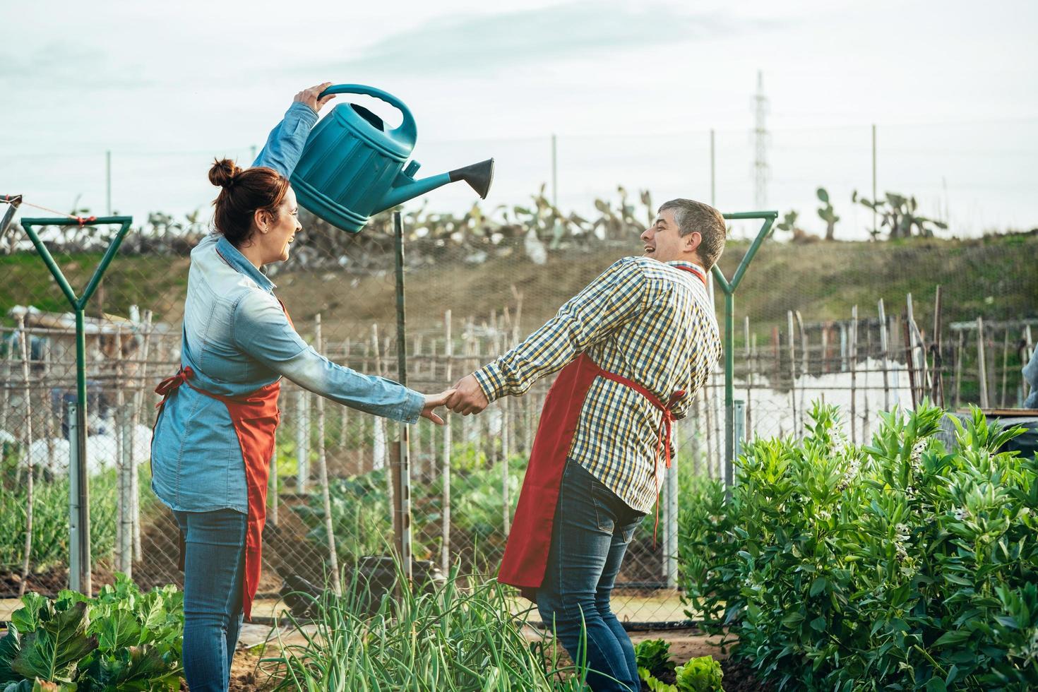 Pareja de agricultores sonriendo y jugando con una regadera en un campo orgánico foto