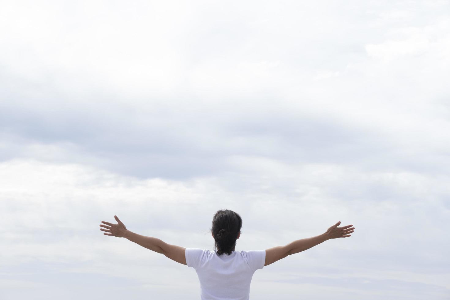 woman in white t-shirt raising her arms facing the sea photo