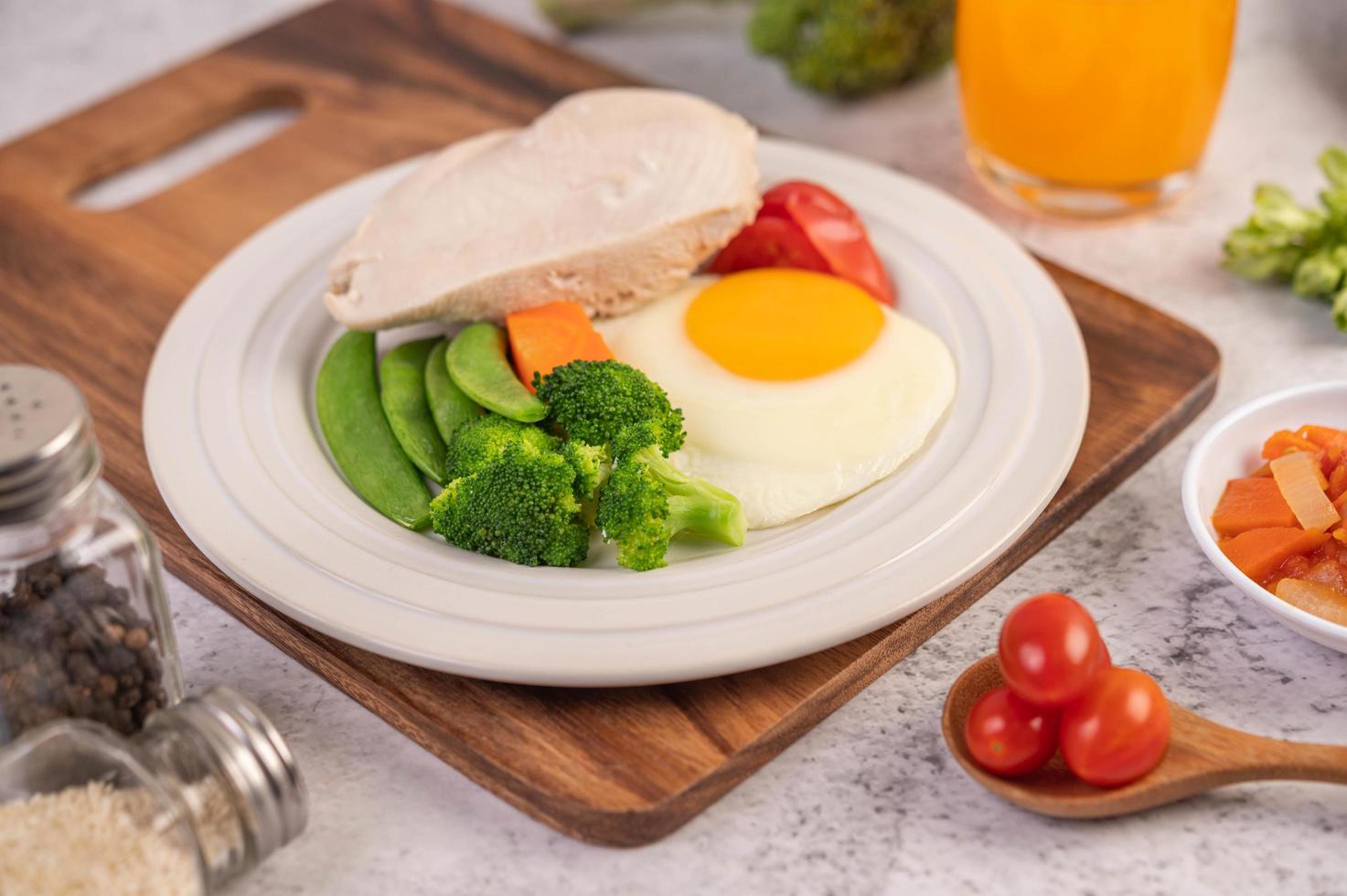 Breakfast spread of chicken, fried eggs, broccoli, carrots, tomatoes and lettuce photo