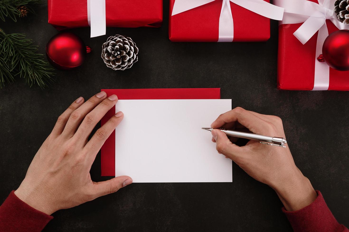 Manos escribiendo maqueta de tarjeta de felicitación blanca con decoración navideña sobre fondo grunge foto