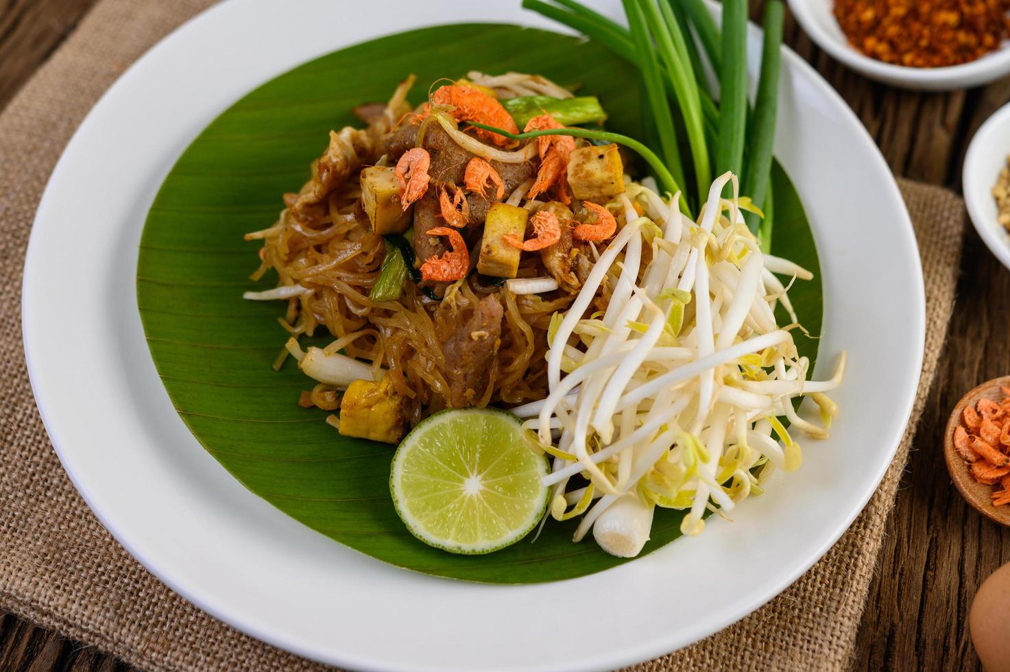 Pad thai con limón, huevos y condimentos sobre una mesa de madera foto