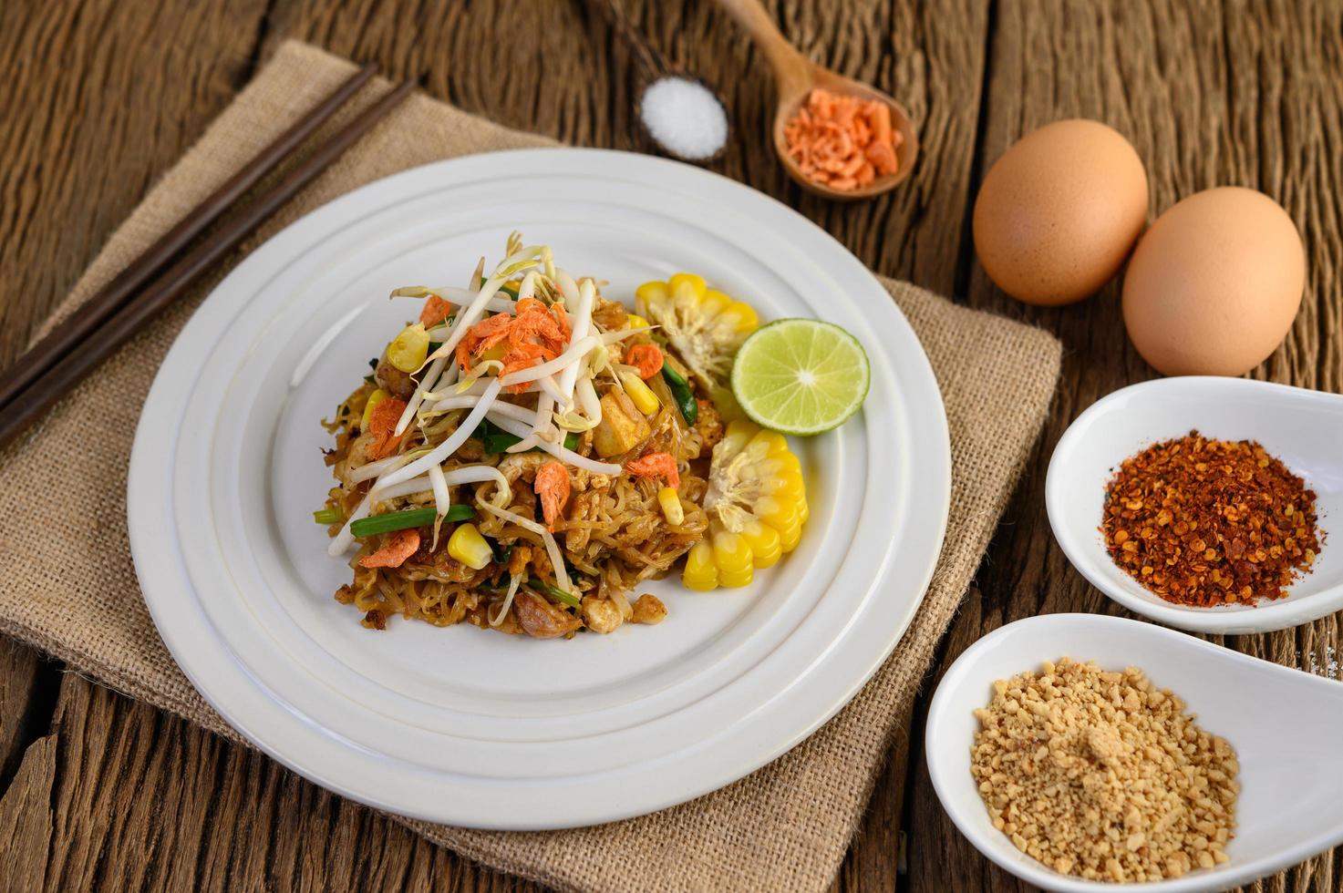 Pad thai con limón, huevos y condimentos sobre una mesa de madera foto