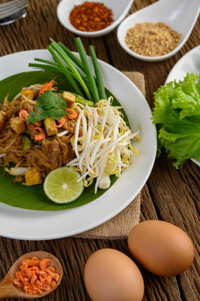 Pad Thai with lemon, eggs and seasoning on a wooden table photo