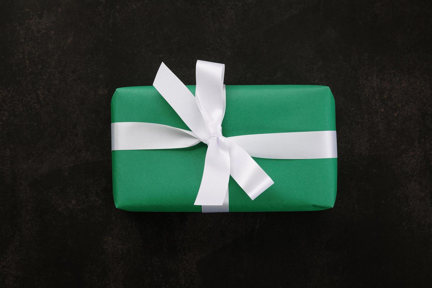Top view of Christmas gift box wrapped with green paper and white ribbon on grunge background photo