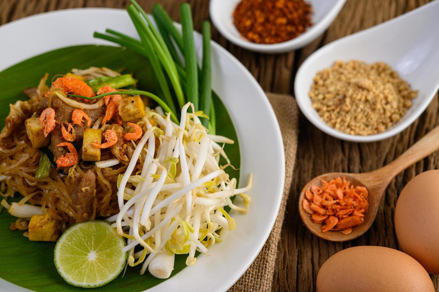 Pad thai con limón, huevos y condimentos sobre una mesa de madera foto