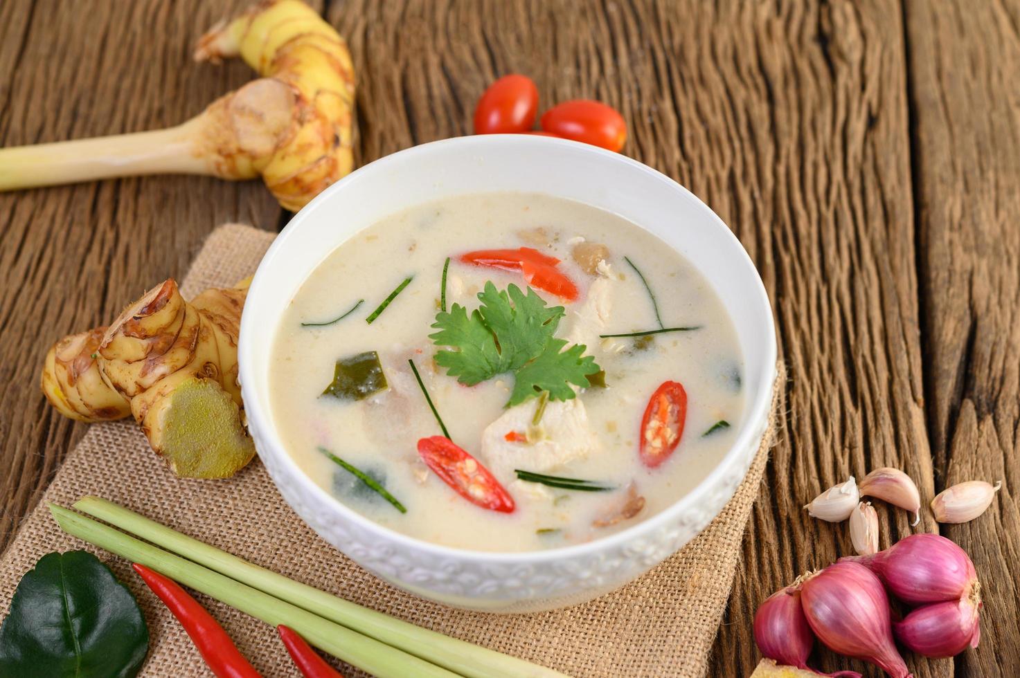 tom kha kai, sopa de coco tailandesa sobre tabla de cocina de madera foto