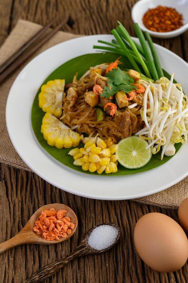 Pad thai con limón, huevos y condimentos sobre una mesa de madera foto