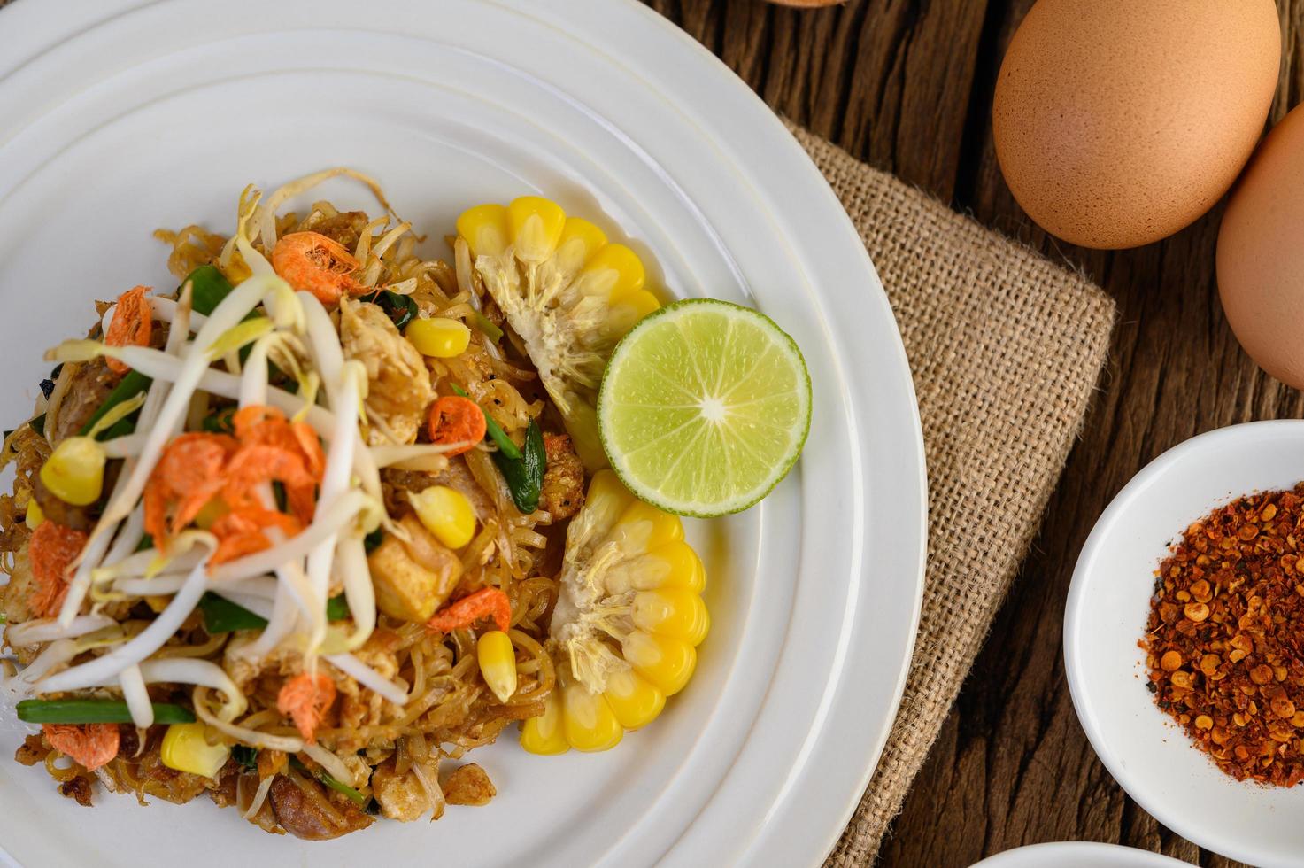 Pad thai con limón, huevos y condimentos sobre una mesa de madera foto