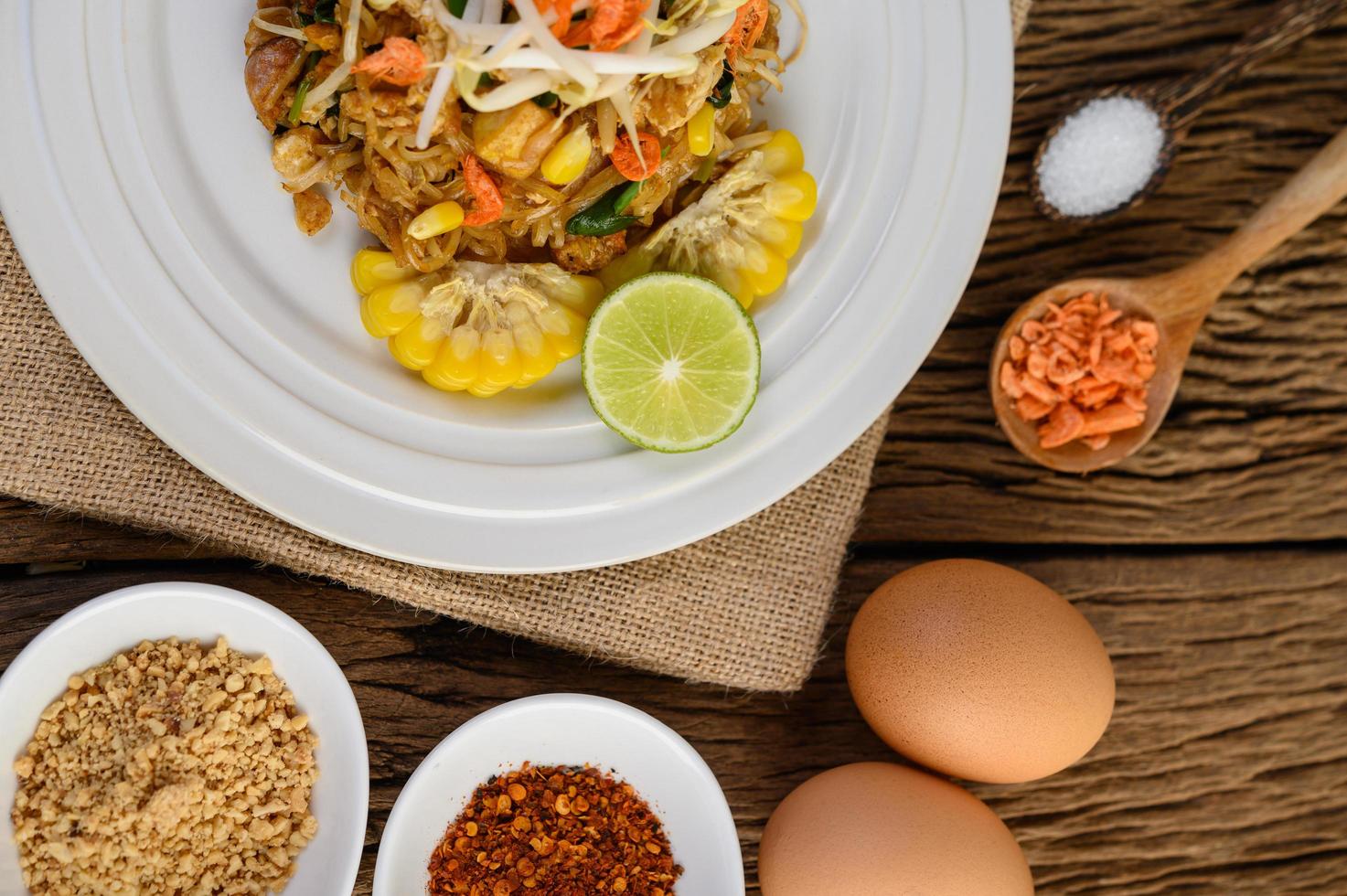 Pad thai con limón, huevos y condimentos sobre una mesa de madera foto