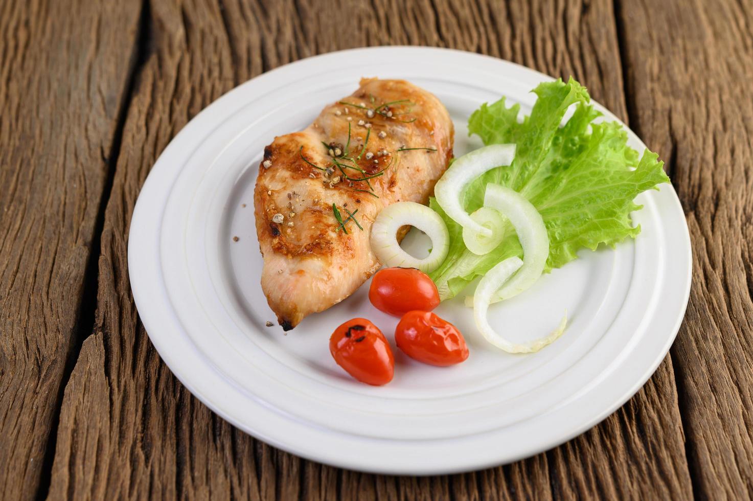 Pollo a la parrilla en un plato con tomate, ensalada y cebolla foto