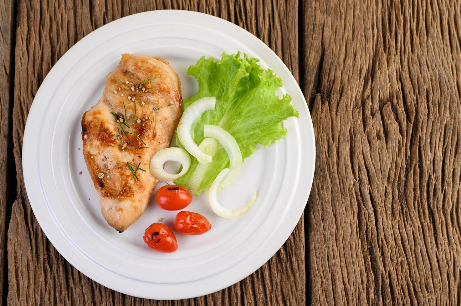 Pollo a la parrilla en un plato con tomate, ensalada y cebolla foto