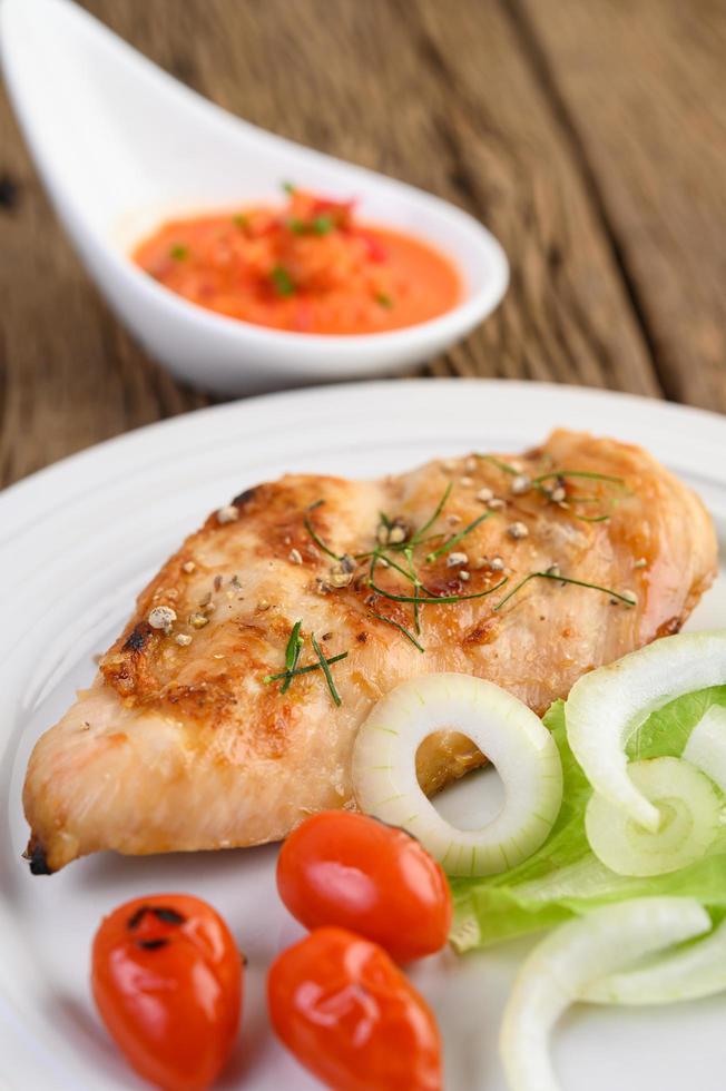 Grilled chicken on a wooden table with tomatoes, salad, onion and chili sauce photo