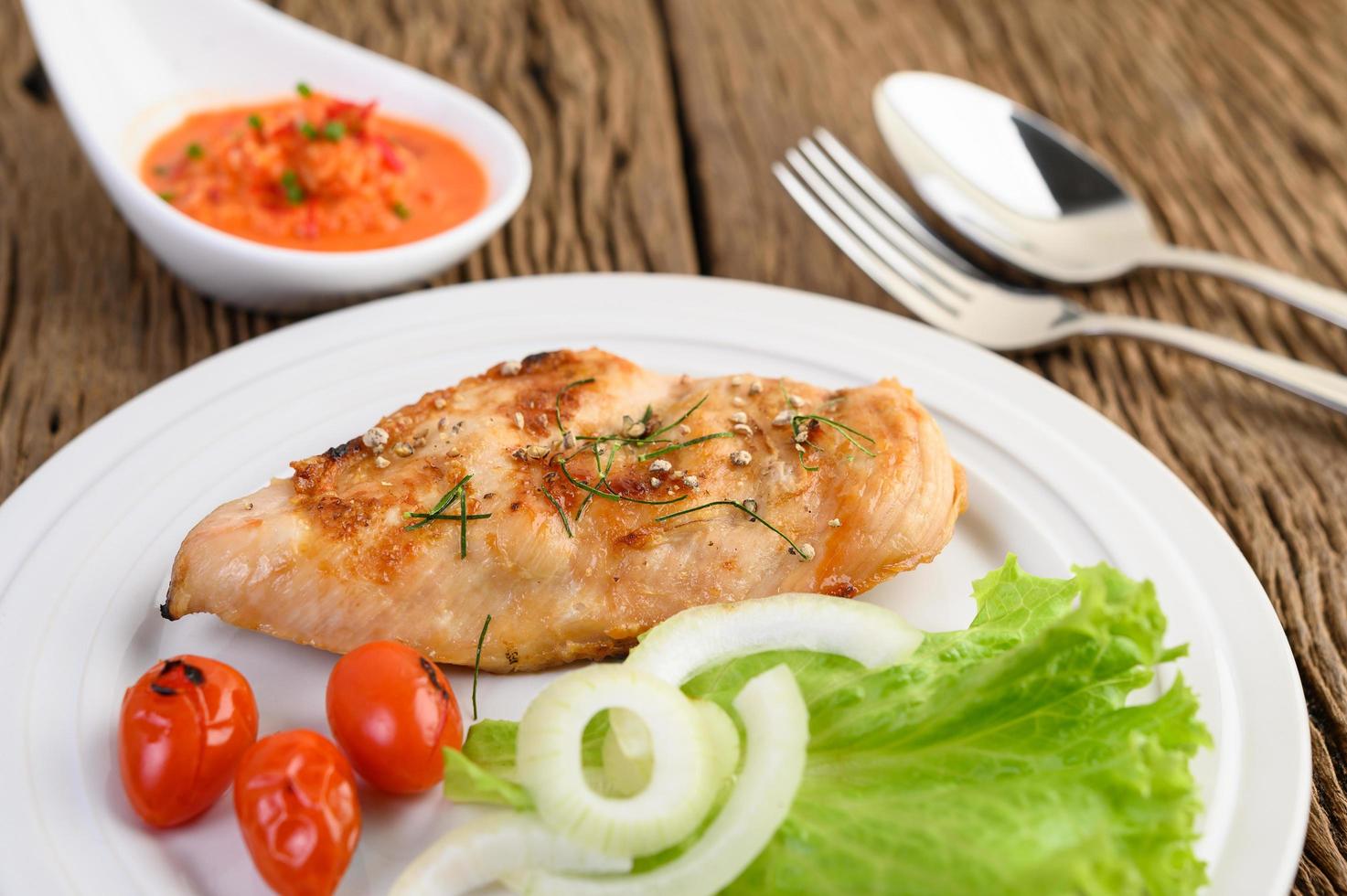 Pollo a la parrilla sobre una mesa de madera con tomate, ensalada, cebolla y salsa de chile foto