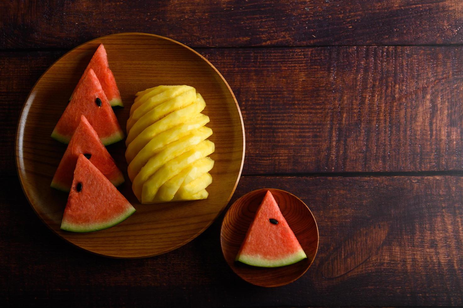 Watermelon and pineapple slices on dark wooden table photo