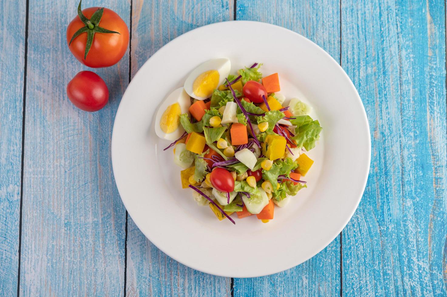 Ensalada fresca en un plato blanco con un sándwich y tomates foto