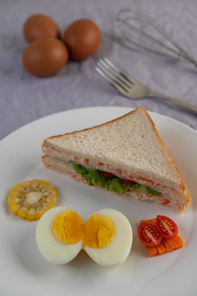 Huevos duros, maíz, sándwich de tomate en un plato blanco foto