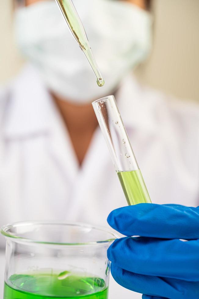 Scientist wearing mask and gloves showing beakers with vaccines photo