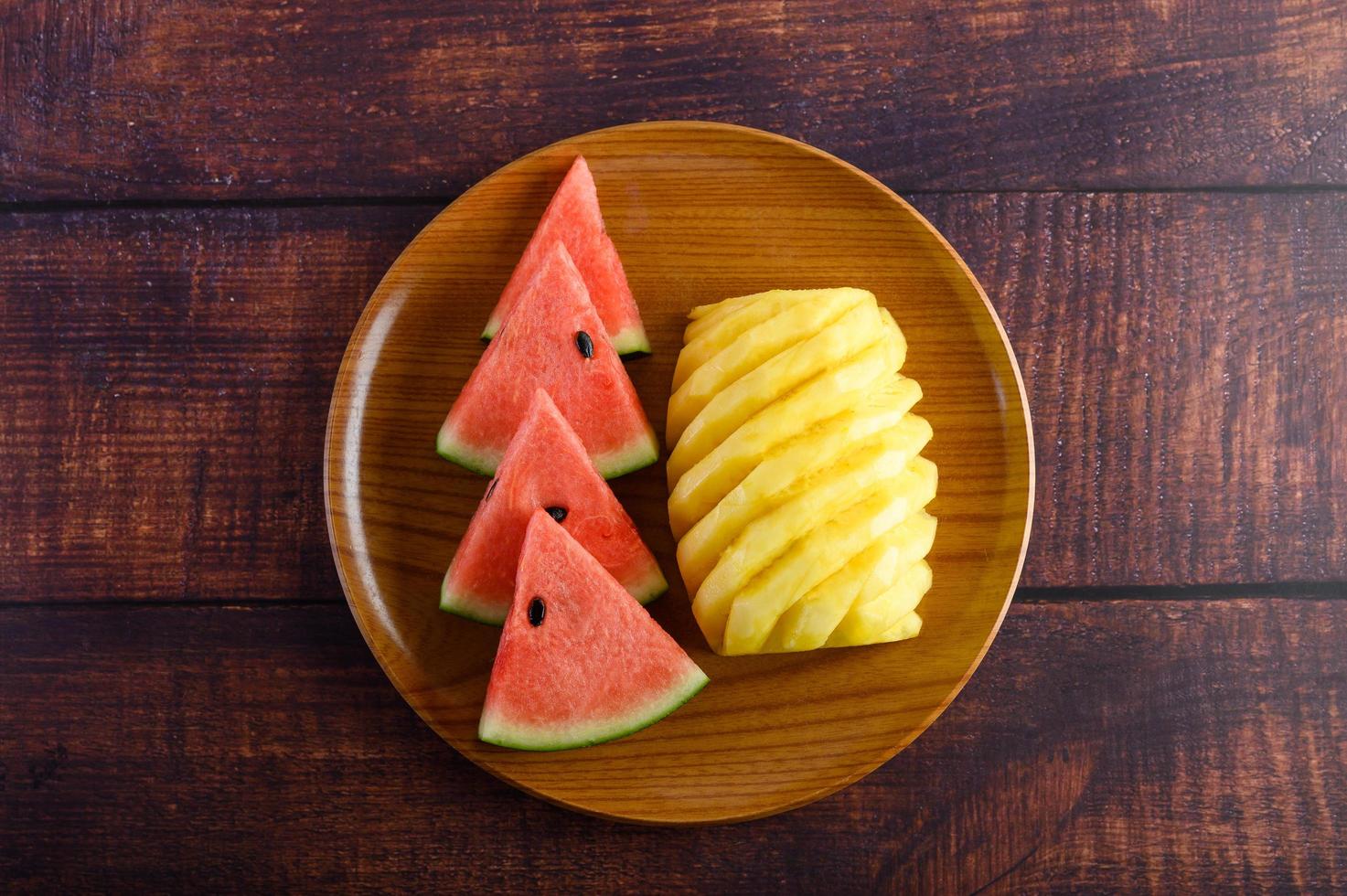 Watermelon and pineapple slices on dark wooden table photo