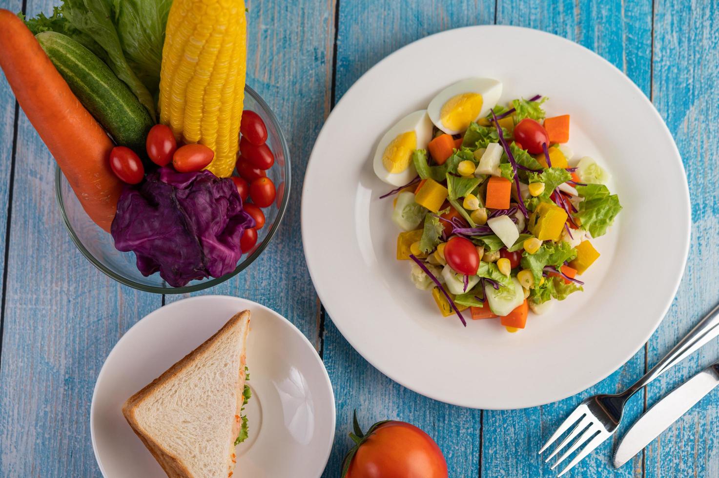 Ensalada fresca en un plato blanco con un sándwich y tomates foto