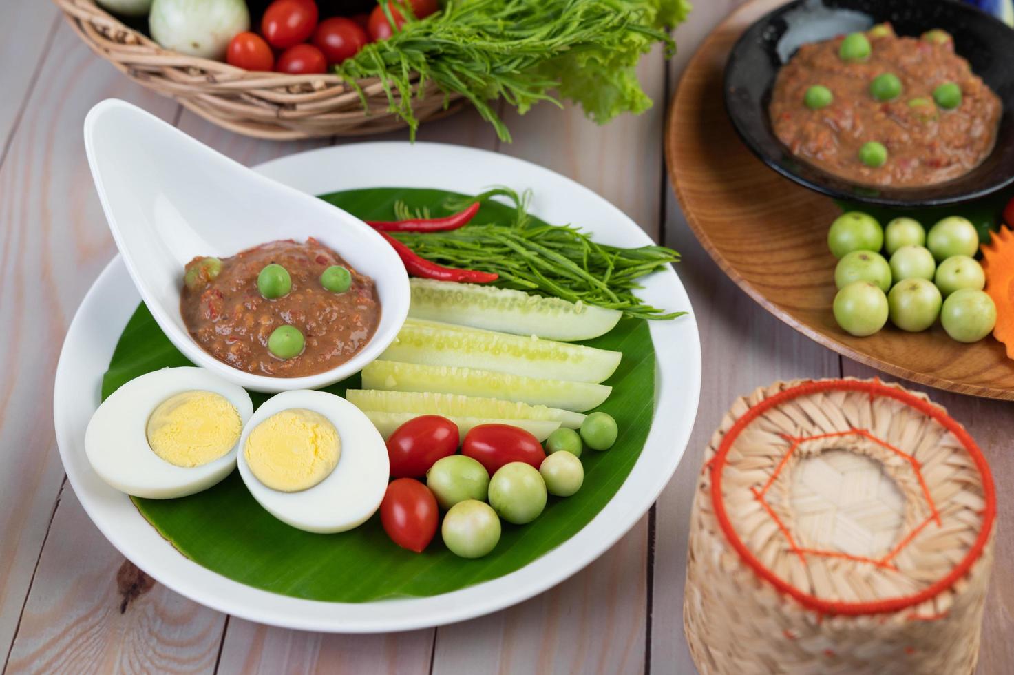 Chili paste paste in a bowl with eggplant, carrots, chili and cucumbers in a basket photo